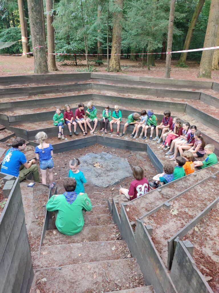 De Welpen zitten in de kampvuurkuil om het lampvuur